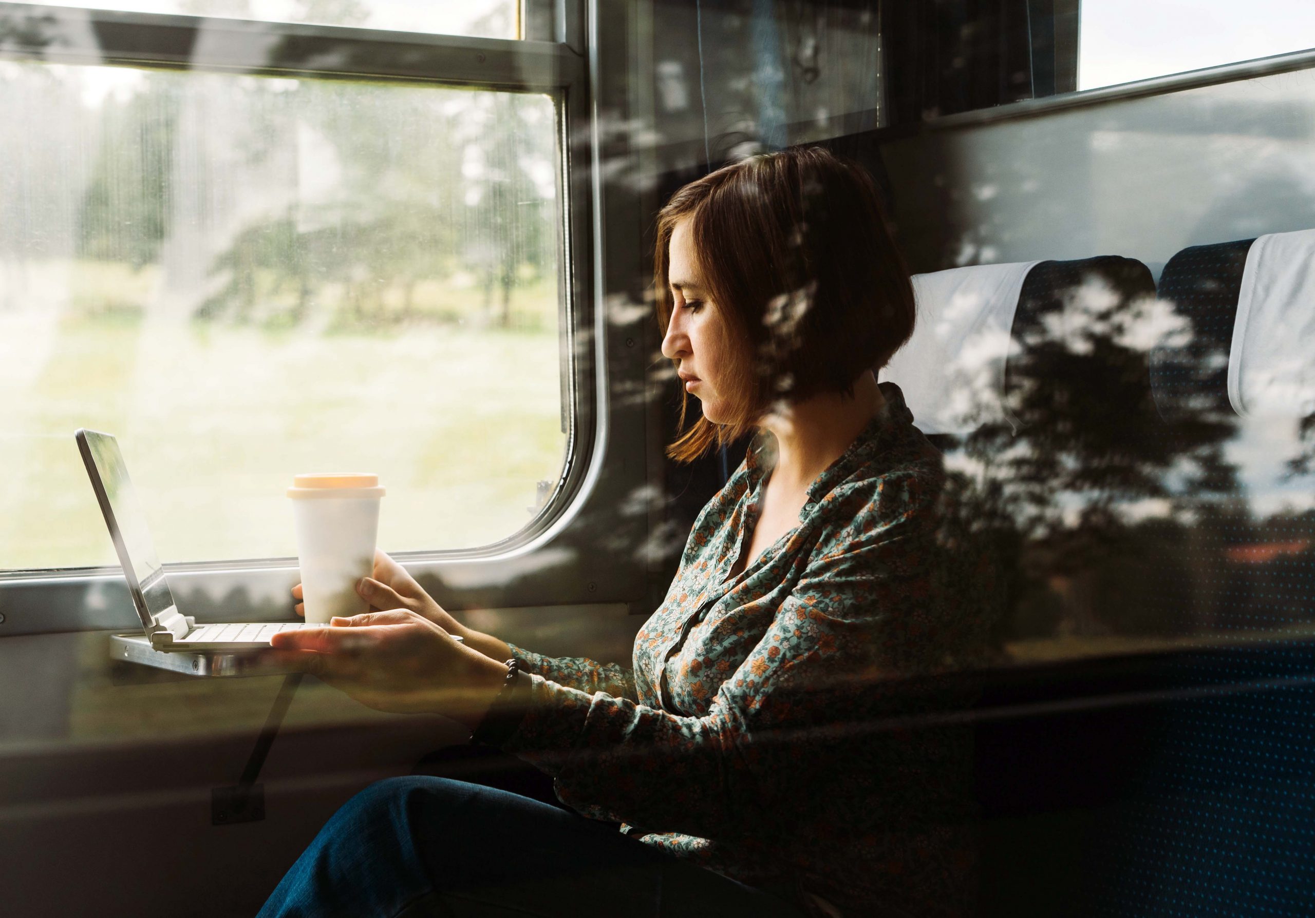 Een vrouw zit in een coupé, drinkt koffie en werkt op haar laptop