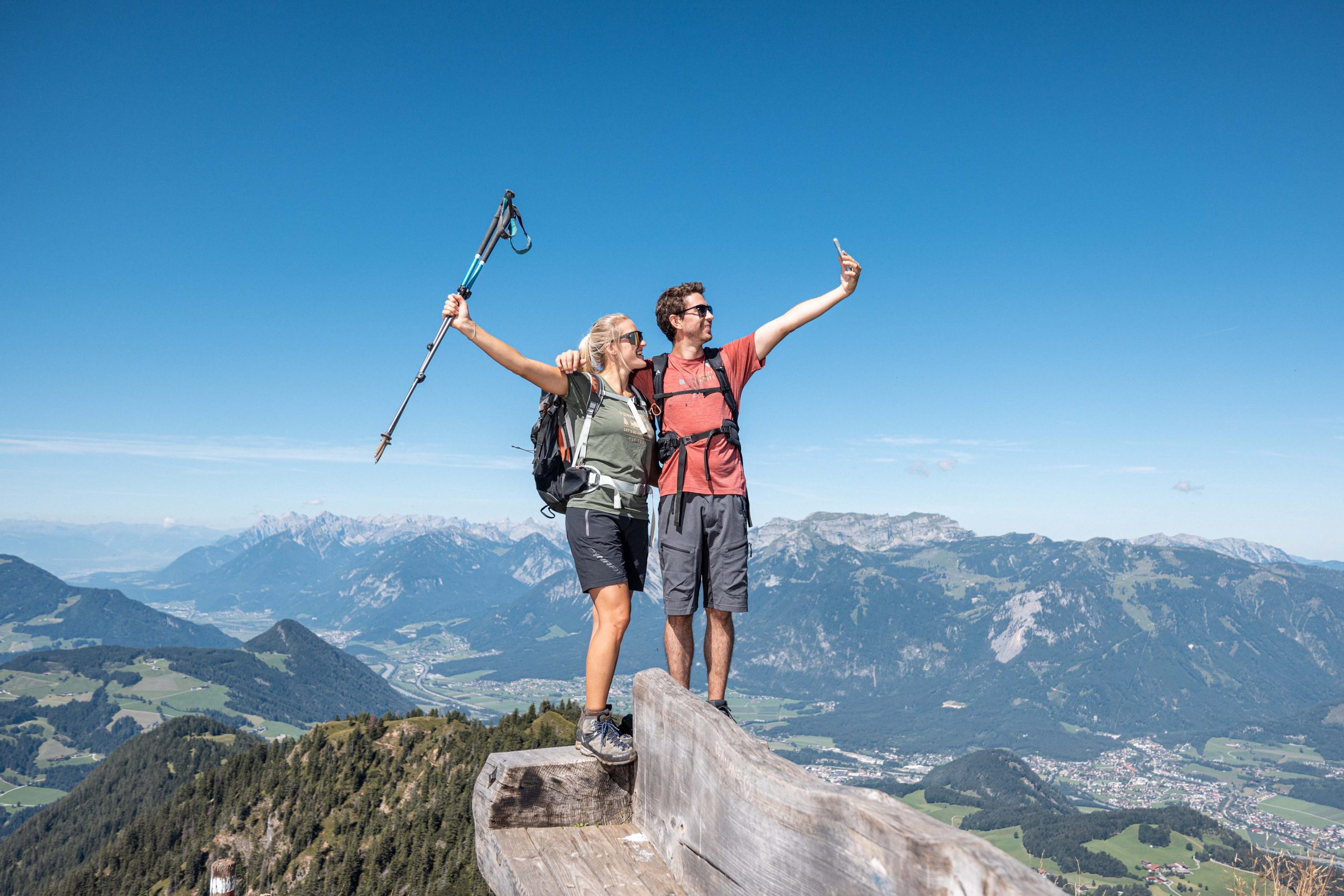 A couple stands on the summit of a mountain in summer and takes a selfie